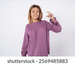 Beautiful teen girl wearing purple dress smiling and confident gesturing with hand doing small size sign with fingers looking and the camera. Measure concept