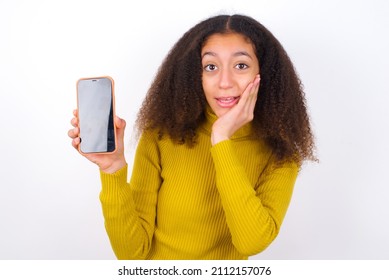 Beautiful Teen Girl Wearing Yellow Turtleneck Sweater Against White Hold Hand Modern Technology Use Touch Face Palm Astonished Impressed Scream Wow Omg Unbelievable Unexpected