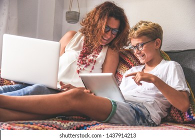 Beautiful teen reading new trend stories online on tablet with mum. Technology addicted young boy watching social video at home with his mother. Child and mommy communicate and plays with tech device.