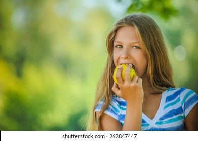 Beautiful teenage girl biting an apple, against green of summer park.