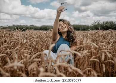 A beautiful teenage girl with long curly hair is taking a selfie on her smartphone in a wheat field. - Powered by Shutterstock