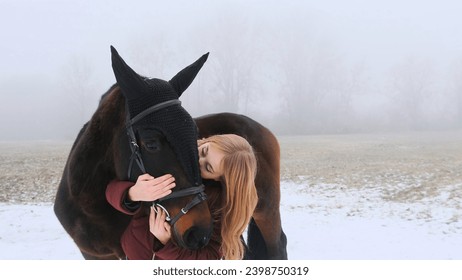 A beautiful teenage girl playfully kisses a brown horse in a foggy field - Powered by Shutterstock