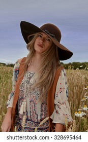 Beautiful teenage girl sitting in a wheat field wearing a floppy hat