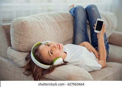 Beautiful teenage girl with smartphone and headphones listening music. Leisure, children, technology and people concept