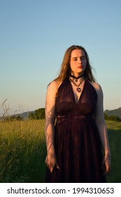 Beautiful Teenage Girl Standing In Tall Grass On A Sunny Spring Night.