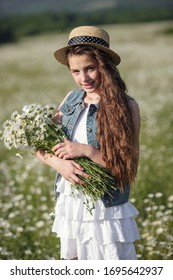 Beautiful teenage girl in a white dress and hat walking in a field of camomiles. Beautiful long and healthy hair. The idea and concept of health and allergies, taking care of yourself