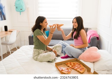 Beautiful teenage girls smiling looking happy while enjoying eating pizza and hanging out together and having fun in the bedroom - Powered by Shutterstock