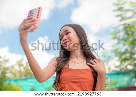 A beautiful teenage lady takes a picture of her gold necklace using the front camera of her phone during the day.