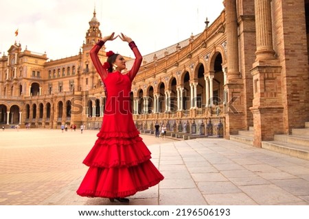 Beautiful teenage woman dancing flamenco in a square in Seville, Spain. She wears a red dress with ruffles and dances flamenco with a lot of art. Flamenco cultural heritage of humanity.