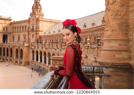Beautiful teenage woman dancing flamenco on the balcony of a square in Seville. She wears a red dress with ruffles with a lot of art. Flamenco cultural heritage of humanity.