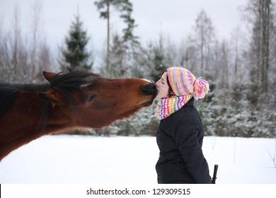 Beautiful teenager girl playfully kissing brown horse in winter forest - Powered by Shutterstock