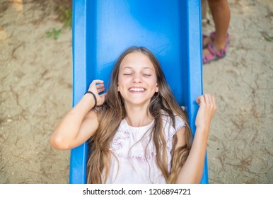 Beautiful teenager lying on blue slide in playground.