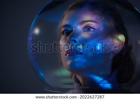 Beautiful tender girl with blue eyes in a glass spacesuit looks into the distance against the background of outer space. Space concept. Copy space. 