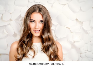 Beautiful tender woman in white dress posing by the background of white paper flowers. Beauty, fashion. Haircare. Cosmetics.
