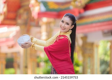 A beautiful Thai woman in Thai dress with gold ornaments holds a cup of water for Songkran Festival or Thai New Year