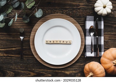 Beautiful Thanksgiving Day holiday place setting with plate, napkin, on a  decorated table shot from flat lay or top view position. Grateful spelled out with wood block letters. Flat lay image.