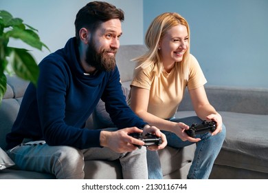 Beautiful Thirties Caucasian Couple, Sitting On Sofa, Smiling And Having Video Game Night.