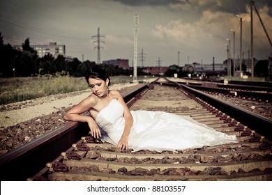 Beautiful thoughtful brunette bride is sitting on the railway and waiting