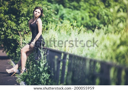 Beautiful thoughtful girl brunette in black dress on fence