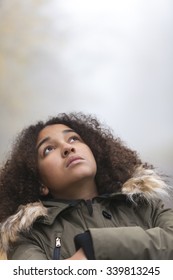 A beautiful thoughtful sad thinking mixed race African American girl or young woman looking up outside on a foggy or misty day