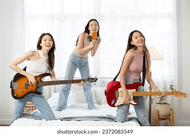 Beautiful three young Asian girls having fun singing and dancing in bedroom. Happy group of Asian friends playing musical instruments guitar bass at home. Friendship leisure rest home enjoy concept - Powered by Shutterstock