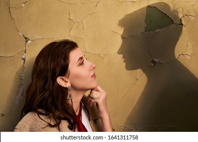 Beautiful througtful young woman thinks of her ideal boyfriend man or lover represented by a shadow on the wall.