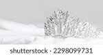 Beautiful tiara on white prom dress against grey background, closeup