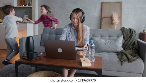 Beautiful Tired Single Mother Trying To Work From Home Using Laptop, Stressed By Two Noisy Running Teenage Children.