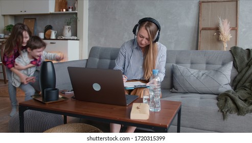 Beautiful Tired Single Mother Trying To Work From Home Using Laptop, Stressed By Two Noisy Running Teenage Children.