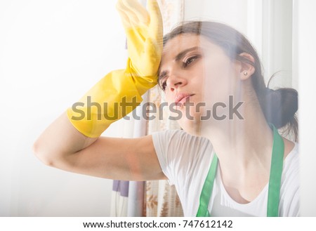 Beautiful tired woman with protective gloves wiping her forehead while cleaning at home