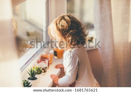 Beautiful toddler with blond hair looks at the candles, staying home because covid