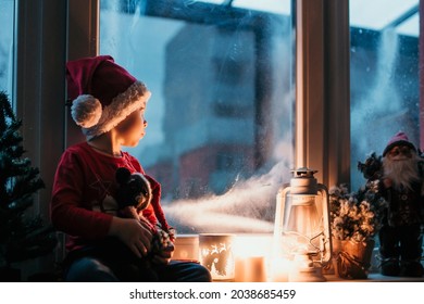 Beautiful toddler child, boy, waiting on the window on Christmas eve, looking for Santa Claus curiously