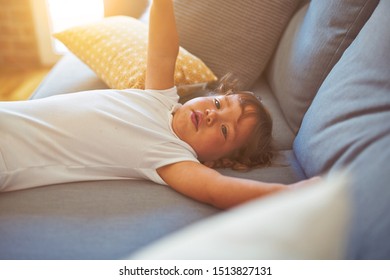 Beautiful toddler child girl wearing white bodysuit lying down on the sofa