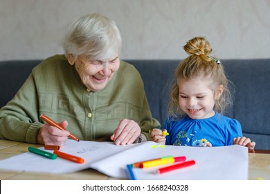 Beautiful Toddler Girl And Grand Grandmother Drawing Together Pictures With Felt Pens At Home. Cute Child And Senior Woman Having Fun Together. Happy Family Indoors