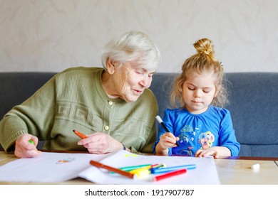 Beautiful Toddler Girl And Grand Grandmother Drawing Together Pictures With Felt Pens At Home. Cute Child And Senior Woman Having Fun Together. Happy Family Indoors