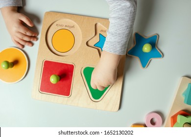 Beautiful toddler play with a wooden frame puzzle geometric figure toys at home. Toddler play with a color educational toy.  Child development.  Baby hands. View from above. Detail.