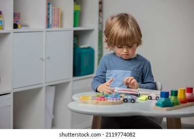 Beautiful Toddler Reading A Book And Playing With A Wooden Toys At Home. Toddler Play With A Color Educational Toy And Wooden Car. Child Play At The Table In The Baby Room. Funny Baby. Lifestyle.