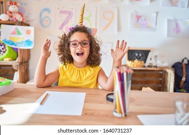 Beautiful Toddler Wearing Glasses And Unicorn Diadem Sitting On Desk At Kindergarten Celebrating Crazy And Amazed For Success With Arms Raised And Open Eyes Screaming Excited. Winner Concept