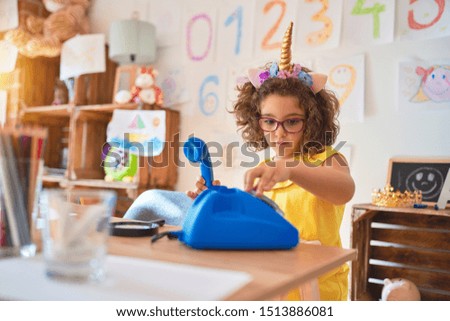 Beautiful toddler wearing glasses and unicorn diadem playing with blue vintage phone at kindergarten