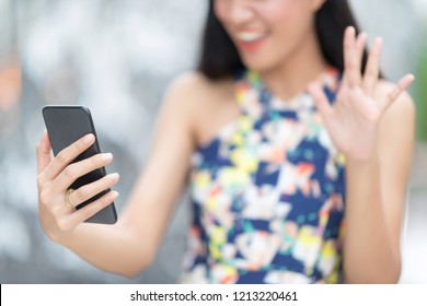 Beautiful Toothy Smiling Young Woman In White Santa's Hat  Using Smartphone Doing FaceTime With Family Against Blur Background.Christmas Concept. Selective Focus At Right Hand.