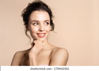 Beautiful Toothy Smiling Young Woman Portrait On Beige Blank Copy Space. Beauty Headshot Of Millennial Pretty Brunette Girl Touching Chin With Hand. Attractive Lady With Naked Shoulder Looking Back