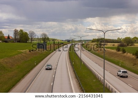Beautiful top view of E4 highway with several cars. Green side fields and stormy sky background. Sweden.