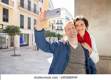 Beautiful Tourist Couple On Sunny Winter City Break Holiday Sightseeing Together, Using Technology Smartphone Smiling, Taking Selfies Outdoors. Fun Travel Vacation, Leisure Recreation Lifestyle.