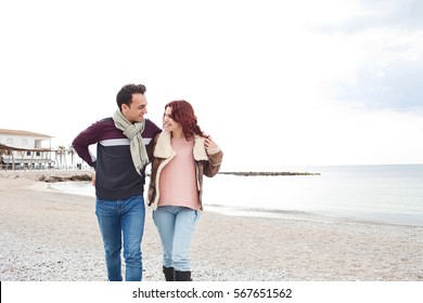 Beautiful Tourist Couple On Winter Break Holiday In Coastal Beach Destination, Walking And Hugging, Recreation Lifestyle Outdoors. Seasonal Travel Vacation. Boyfriend And Girlfriend Smiling Together.