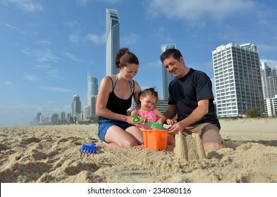 Beautiful tourist family of father and mother with young daughter girl are  building a sand castle together on Surfers Paradise main beach in Gold Coast Queensland, Australia. Real people. Copy space