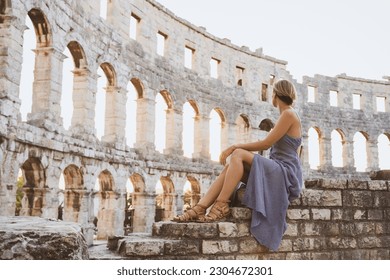 Beautiful tourist woman in Roman Amphitheater Arena like Coliseum - famous travel destination in Pula, Croatia. Female traveler visiting the sights. Vacation in Europe at summertime.
