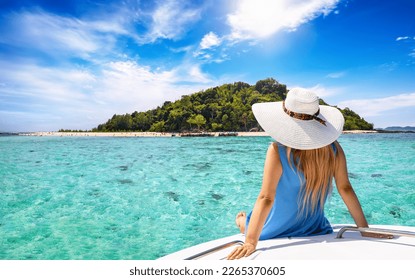 A beautiful tourist woman with sunhat sits on a yacht and looks at the turquoise sea and beaches of Bamboo island in the Krabi region, Thailand