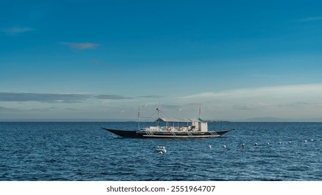 A beautiful traditional double-outrigger dugout bangka boat is anchored in the blue ocean. Life buoys on the railing. The awning over the deck. Ripples on the water. azure sky, clouds. Philippines. - Powered by Shutterstock