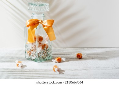 Beautiful transparent glass mason jar with orange bow and a few caramel candies on light background. 