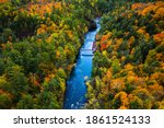 Beautiful travel aerial of a pedestrian foot bridge crossing the bright blue water of the Bad River  at Copper Falls with colorful fall foliage lining the river banks in autumn in Mellen, Wisconsin.